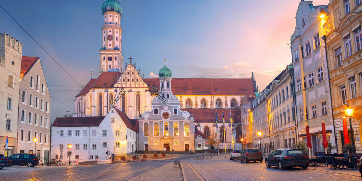 Augsburg, Deutschland. Stadtbild der Altstadtstraße von Augsburg, Deutschland mit der Basilika St. Ulrich und Afra bei Herbstsonnenuntergang.