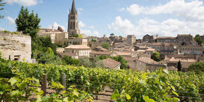 einberge und historische Altstadt von Saint-Émilion bei Bordeaux, Frankreich, mit Kirchturm und Sandsteinbauten unter blauem Himmel.