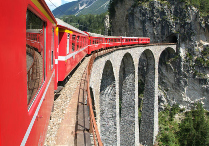 Busreisen in die Schweiz. Roter Bernina-Express auf dem Landwasserviadukt in Graubünden, Schweiz, bei sonnigem Wetter mit Blick in die Schlucht.