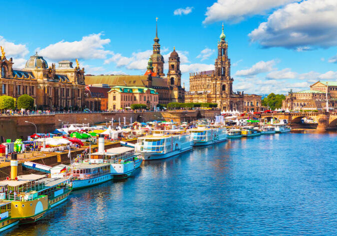Blick auf die historische Altstadt von Dresden, Deutschland, mit Elbufer, Anlegestellen und barocker Architektur unter blauem Himmel.