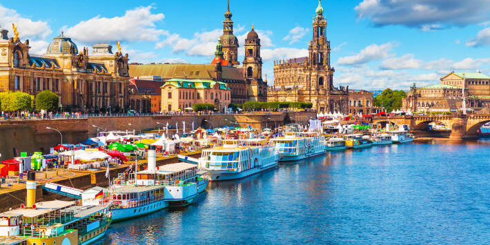 Blick auf die historische Altstadt von Dresden, Deutschland, mit Elbufer, Anlegestellen und barocker Architektur unter blauem Himmel.