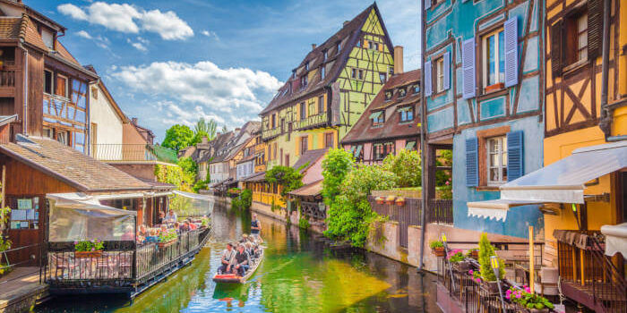 Elsass_141484417 Fachwerkhäuser am Kanal in der Altstadt von Colmar, Elsass, Frankreich, mit Boot und blühenden Balkonen bei sonnigem Wetter.