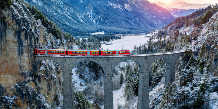 Roter Glacier-Express auf dem Landwasserviadukt in der verschneiten Winterlandschaft der Schweizer Alpen bei Sonnenuntergang.