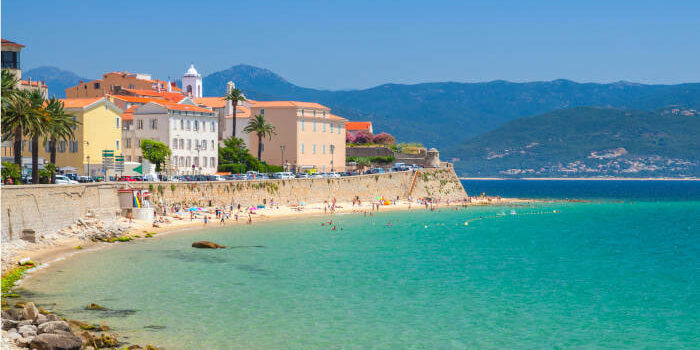 Strand und Altstadt von Ajaccio auf Korsika, Frankreich, mit türkisblauem Meer und Bergkulisse im Hintergrund.