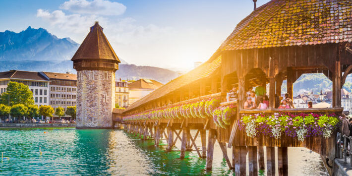 Luzern Schweiz Reisen. Kapellbrücke mit Wasserturm in Luzern, Schweiz, bei Sonnenuntergang und blumengeschmücktem Geländer über der Reuss.