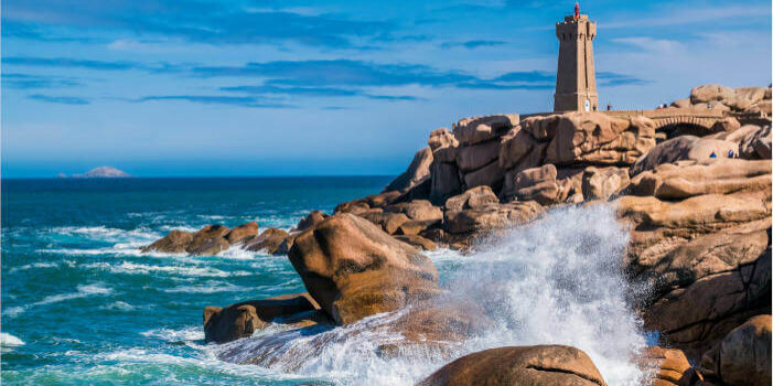 Phare de Mean Ruz bei Ploumanac’h in der Bretagne, Frankreich, mit rosa Granitfelsen und Wellen, die gegen die Küste schlagen.