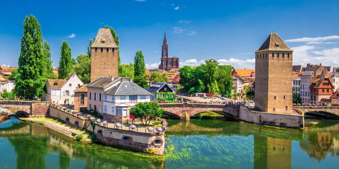 Historische Ponts Couverts in Straßburg, Elsass, Frankreich, mit Türmen, Brücken und Spiegelung im Fluss Ill bei sonnigem Wetter.