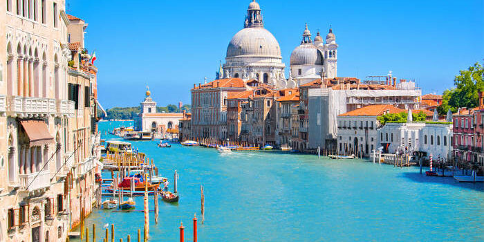 Venedig_40281519 Grand Canal in Venedig, Italien, mit der Kirche Santa Maria della Salute und historischen Palästen bei blauem Himmel.